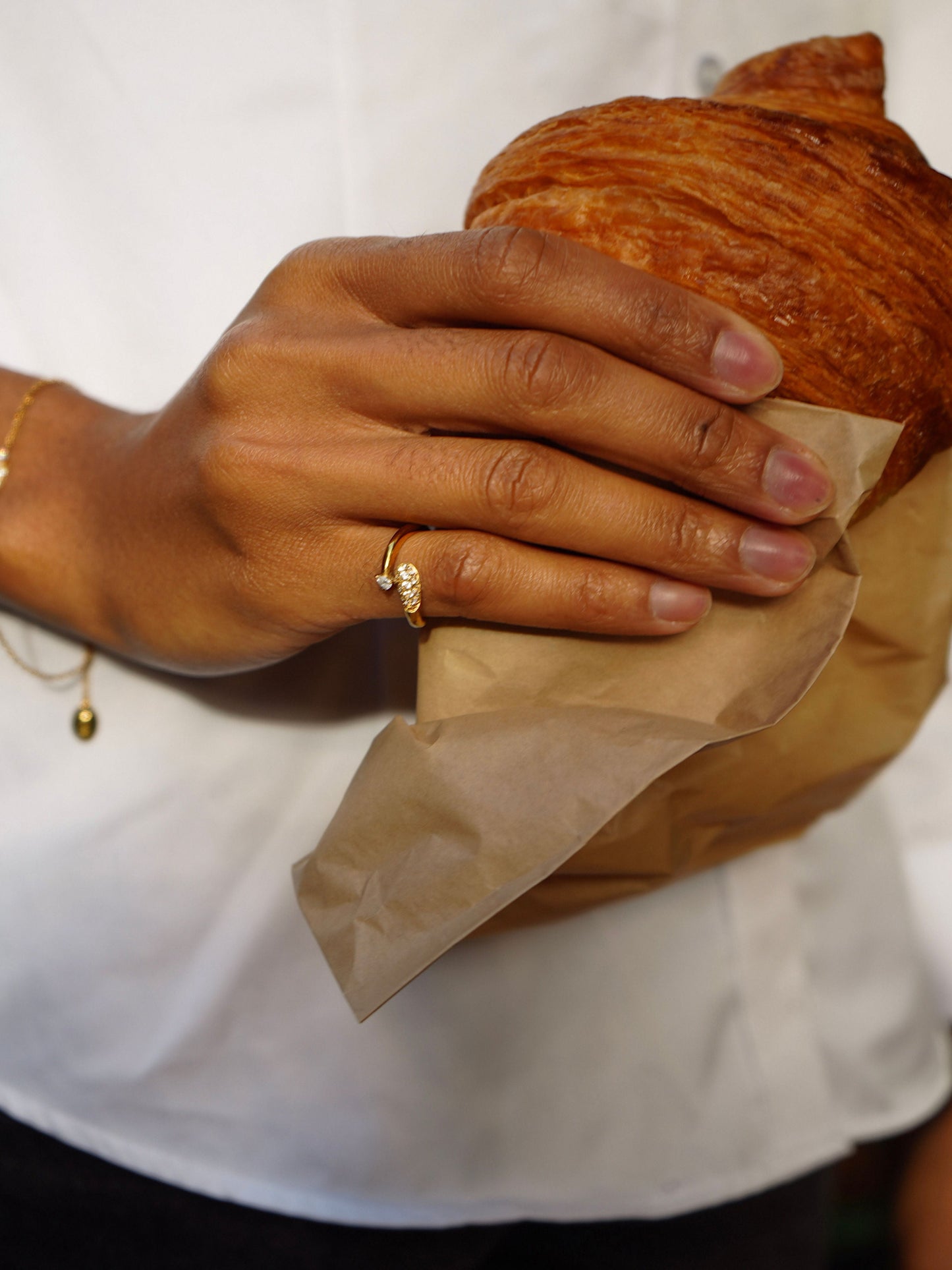 Hand holding a golden croissant, featuring a delicate gold ring with a sparkling detail.